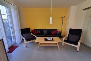 Olohuone, jossa on sohva, kaksi nojatuolia, sohvapöytä ja lattiavalaisin.