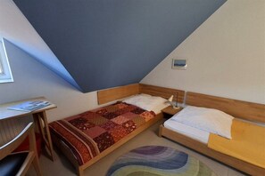 Une petite pièce triangulaire comprenant deux lits, un bureau et une fenêtre.