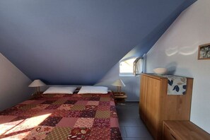 A bedroom with a sloped ceiling, a quilted bedspread, two bedside lamps, a wooden nightstand, and a window with daylight. - Holiday apartment with 2 bedrooms (Kaltenhof (Insel Poel))