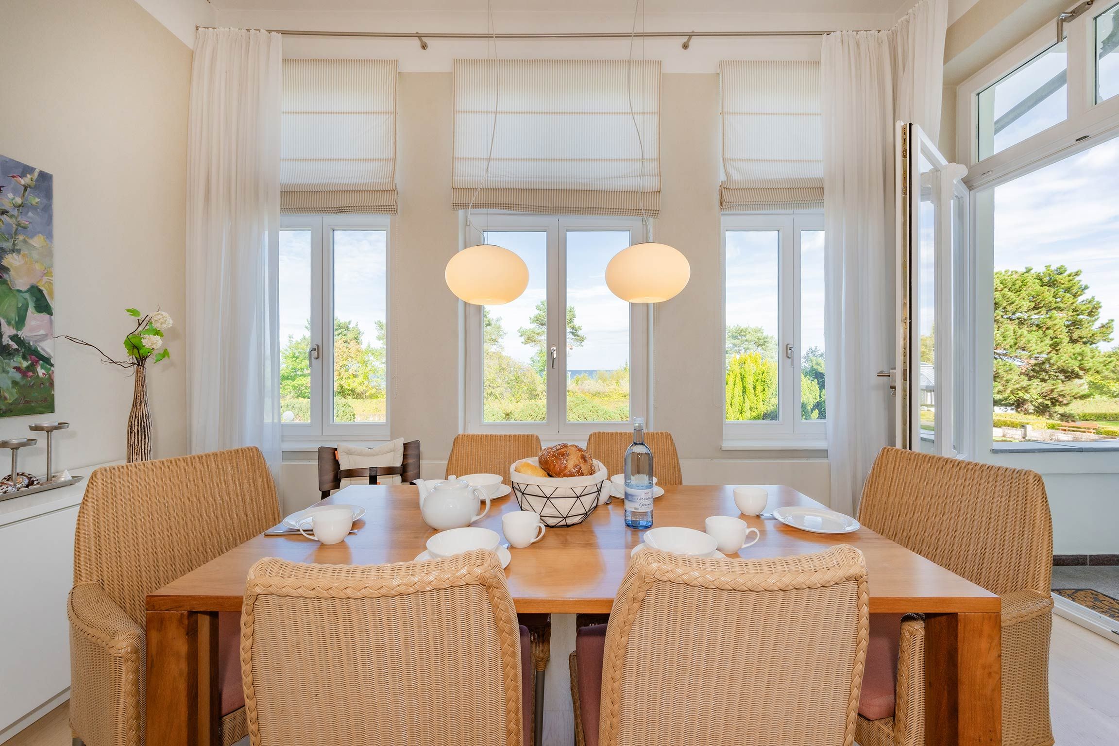 Un coin repas avec une table en bois, des chaises en osier et une vue sur la verdure environnante.