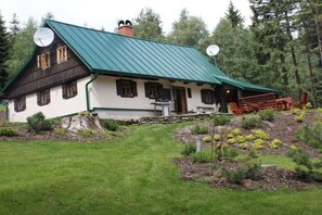A traditional house with a green roof, a stone foundation, and a small porch with wooden furniture. - Alpine cabin with 3 bedrooms (Horní Maršov)