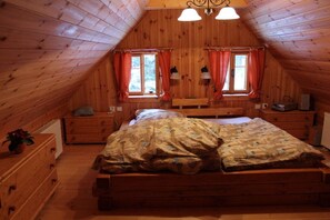 A wooden-paneled attic bedroom with a bed, two bedside tables, a bench, and two windows with curtains. - Alpine cabin with 3 bedrooms (Horní Maršov)
