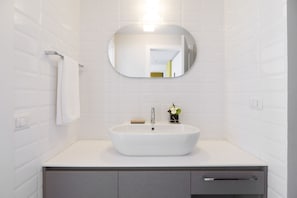 A bathroom with a white sink, a round mirror, and a towel hanging on a rack. - Vrbo Property (Milano)