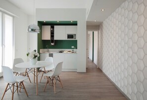 A modern kitchen with white cabinetry, a green accent wall, and a dining area with white chairs and a table. - Contempora - Cavallotti 13 - Two-room apartment with a terrace on the top floor - A64 (Milano)