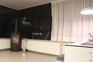 A room with a black heater, a white radiator, a TV mounted on the wall, and a white curtain. - Beach House Dune Nest (Fehmarn)