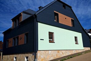 Ein zweistöckiges Haus mit steinernen Fundament, geneigtem Dach und einer Mischung aus dunklen und hellen Außenwänden.