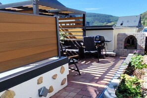 Eine Terrasse im Freien mit einer Holz-Pergola, einem Grill und einer Steinmauer.