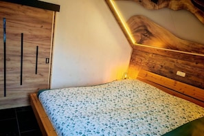 Ein Schlafzimmer mit einem hölzernen Kopfteil, einem Bett mit floralem Bettbezug und einer geneigten Decke.
