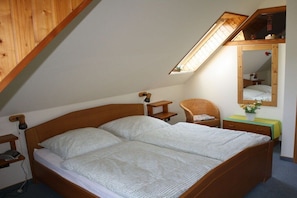 Une chambre avec un plafond en pente, un lit en bois, une table de chevet, une chaise, une petite table avec une lampe et un miroir.