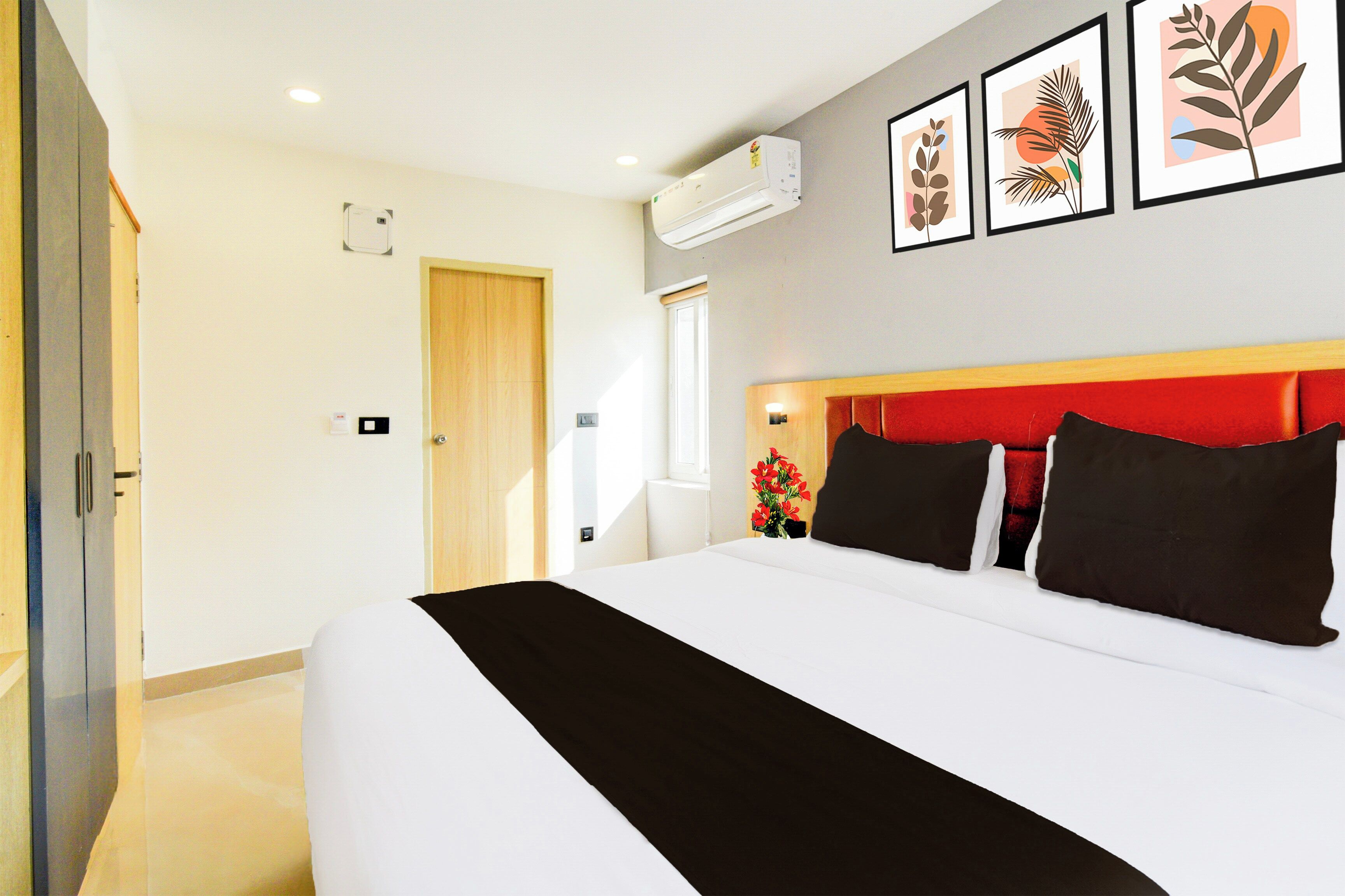 Quarto de hotel com uma cama grande, porta de madeira, ar condicionado e quadros na parede.