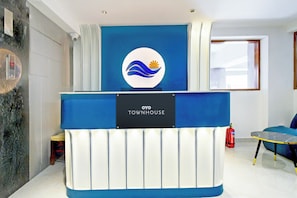 A reception desk with a logo and 'OYO TOWNHOUSE' signage, a fire extinguisher, and a window with blinds. - Townhouse Aarav Business Hotel  (Hyderabad)