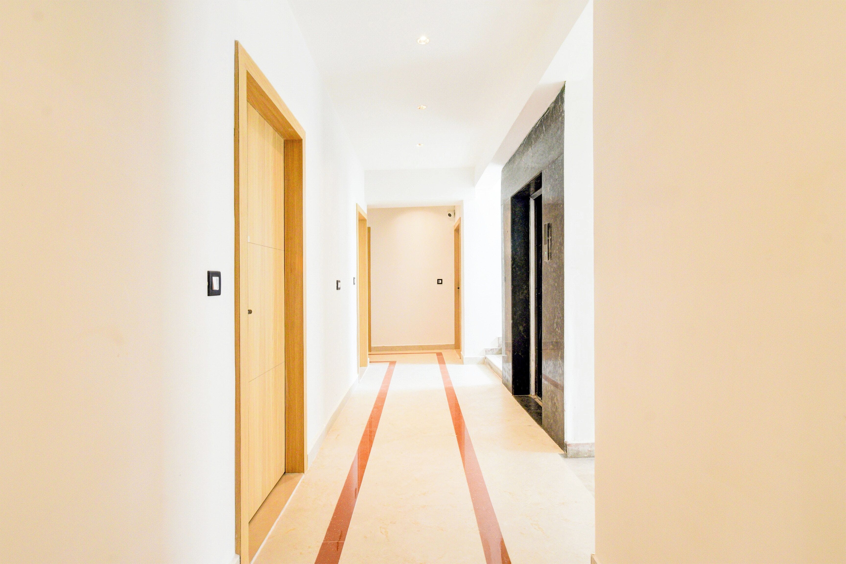 Un pasillo con una puerta de madera a la izquierda, una pared blanca y una puerta negra a la derecha.