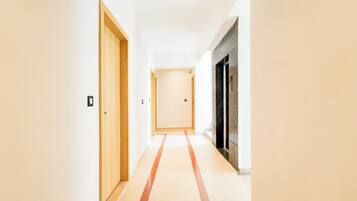 Un pasillo con una puerta de madera a la izquierda, una pared blanca y una puerta negra a la derecha.