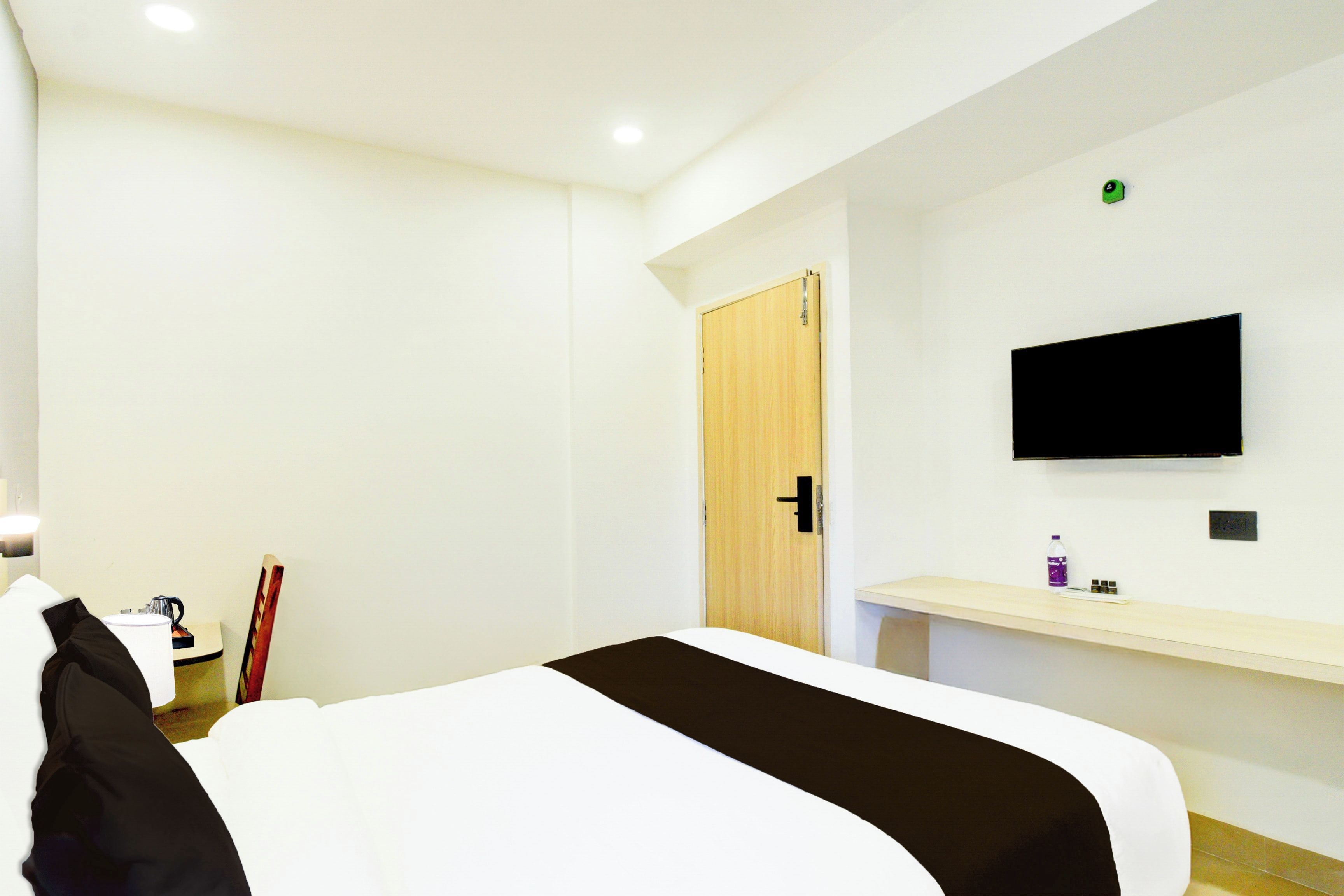 Una habitación de hotel con cama, escritorio, televisor montado en la pared y una puerta.