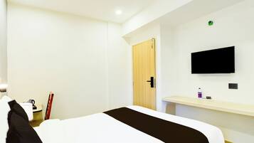 Una habitación de hotel con cama, escritorio, televisor montado en la pared y una puerta.