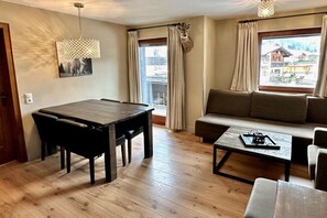 Een kamer met een eettafel, stoelen, een bank, een salontafel en een raam met gordijnen.