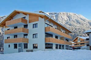 Un immeuble à plusieurs étages, doté de balcons, se dressant sur fond de montagnes enneigées.