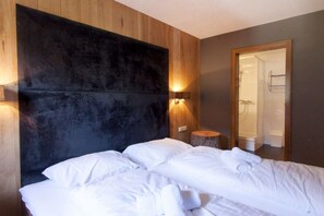A hotel room with a large bed, a wooden headboard, a wall-mounted light, and a mirror reflecting a bathroom. - Apartment Laijola III (Gaschurn)