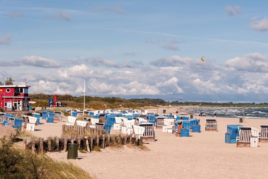 Une plage avec de nombreuses cabanes de plage, un bâtiment rouge et des éoliennes en arrière-plan.