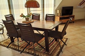 A dining area with a table, chairs, a lamp, and a television in the background. - "Sea Breeze", 50 m from the beach (Insel Poel \/Schwarzer Busch)