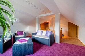 A room with a high ceiling, a bed, a sofa, a coffee table, and a large plant. - Holiday apartment with 4 bedrooms (Hohnstein)