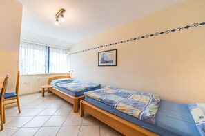 A room with two wooden beds, a chair, a radiator, and a window with curtains. - Holiday home with 2 bedrooms (Kaltenhof)
