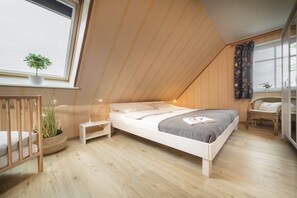 Ein Schlafzimmer mit schrägen Wänden, einem Bett, einem Nachttisch, einem Sessel, einem Fenster mit Aussicht und einer Topfpflanze.
