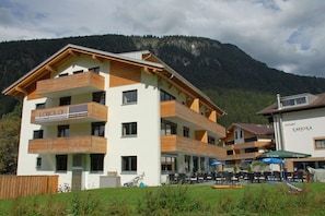 A multi-story hotel with balconies, outdoor seating, and a mountain backdrop. - Apartment Laijola II (Gaschurn)