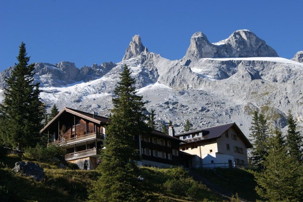 Un chalet de montagne à l’extérieur en bois, doté de plusieurs balcons et offrant une vue sur des sommets enneigés.