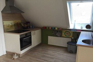 A compact kitchen with a stove, oven, and a window with blinds. - Holiday apartment with 1 bedroom (Fehmarn)