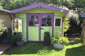 A small, green and purple shed with a door and windows, surrounded by potted plants and a garden. - Holiday apartment with 1 bedroom (Fehmarn)