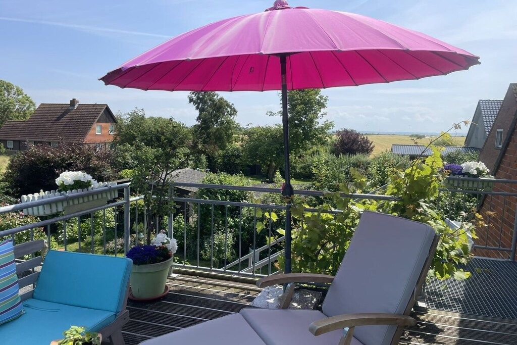 A balcony with a pink umbrella, two lounge chairs, and potted plants.