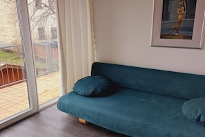 En teal farvet sofa med puder, et billede i ramme på væggen og udsigt gennem en skydedør.
