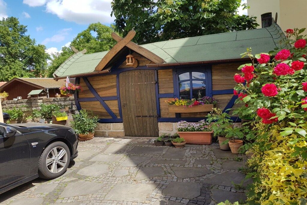 A rustic cabin with a stone-paved entrance, wooden walls, and a green roof.