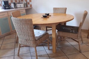 Ein runder Holztisch mit vier Korbstühlen, einer Kaffeemaschine und einem Toaster auf der Arbeitsplatte.