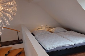 Et soveværelse med en seng, et natbord, en vægmonteret lampe og en trappe.