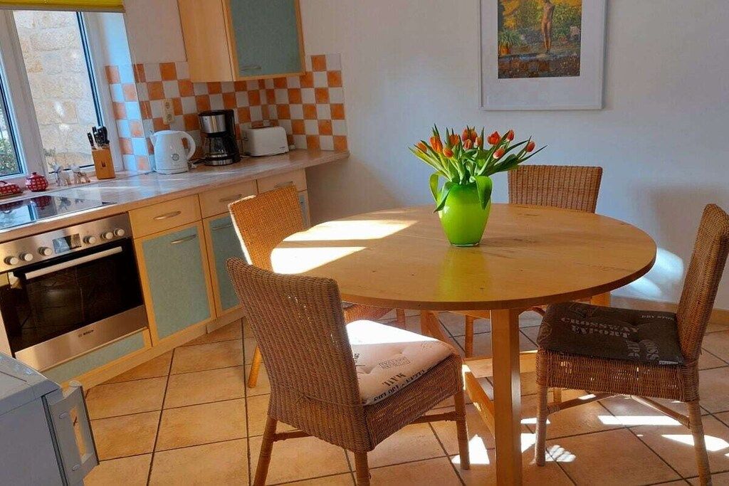 A kitchen with a round dining table, wicker chairs, and a green vase with flowers.