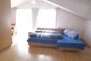 Ein Einzelbett mit blauer Bettdecke und passenden Kissen in einem Zimmer mit Holzboden und geneigter Decke.