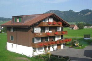 Ein mehrstöckiges Gebäude mit Balkonen, einer kleinen Gartenanlage und Blick auf die umliegende Landschaft.
