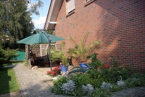 Ein Backsteinhaus mit überdachter Terrasse, Blumentöpfen und einem Weg zum Eingang.