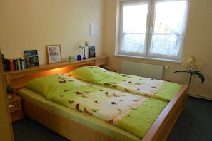 Ein Schlafzimmer mit einem Bett, Nachttischen, einem Fenster und einer Heizung.