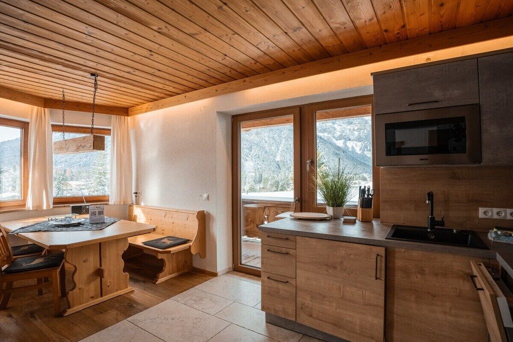 Une cuisine moderne avec des armoires en bois, un four à micro-ondes encastré et une grande fenêtre donnant sur l’extérieur.