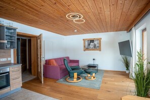 A modern living room with a wooden ceiling, a sofa, a chair, a small table, and a television. - Most stylish sky lodge (Leutasch)