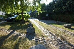 Ein gepflasterter Weg mit großen Steinen, ein parkendes Auto und ein Gebäude im Hintergrund.