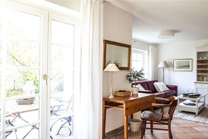 Ein Zimmer mit Schreibtisch aus Holz, einem violetten Sofa, einem Spiegel und einem Fenster mit Vorhängen.