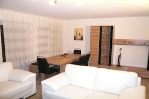 A modern living room with a dining table, two white sofas, and a glass cabinet. - Holiday apartment with 3 bedrooms (Sierksdorf)