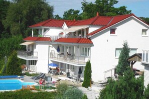 A two-story building with a red-tiled roof, a swimming pool, and outdoor seating. - Holiday apartment with 3 bedrooms (Sierksdorf)