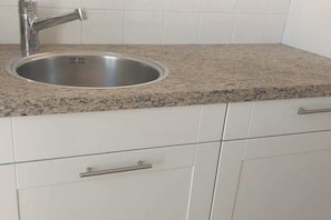 Eine Küche mit Spüle aus Edelstahl, einer Arbeitsplatte aus Granit und weißen Schränken.