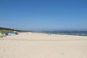 Ein Strand mit Zelten und Menschen, strahlend blauem Himmel und ruhiger See.