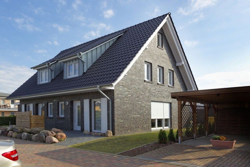 Une maison moderne à deux étages, dotée d’un toit en pente, d’un patio couvert et d’une allée pavée.